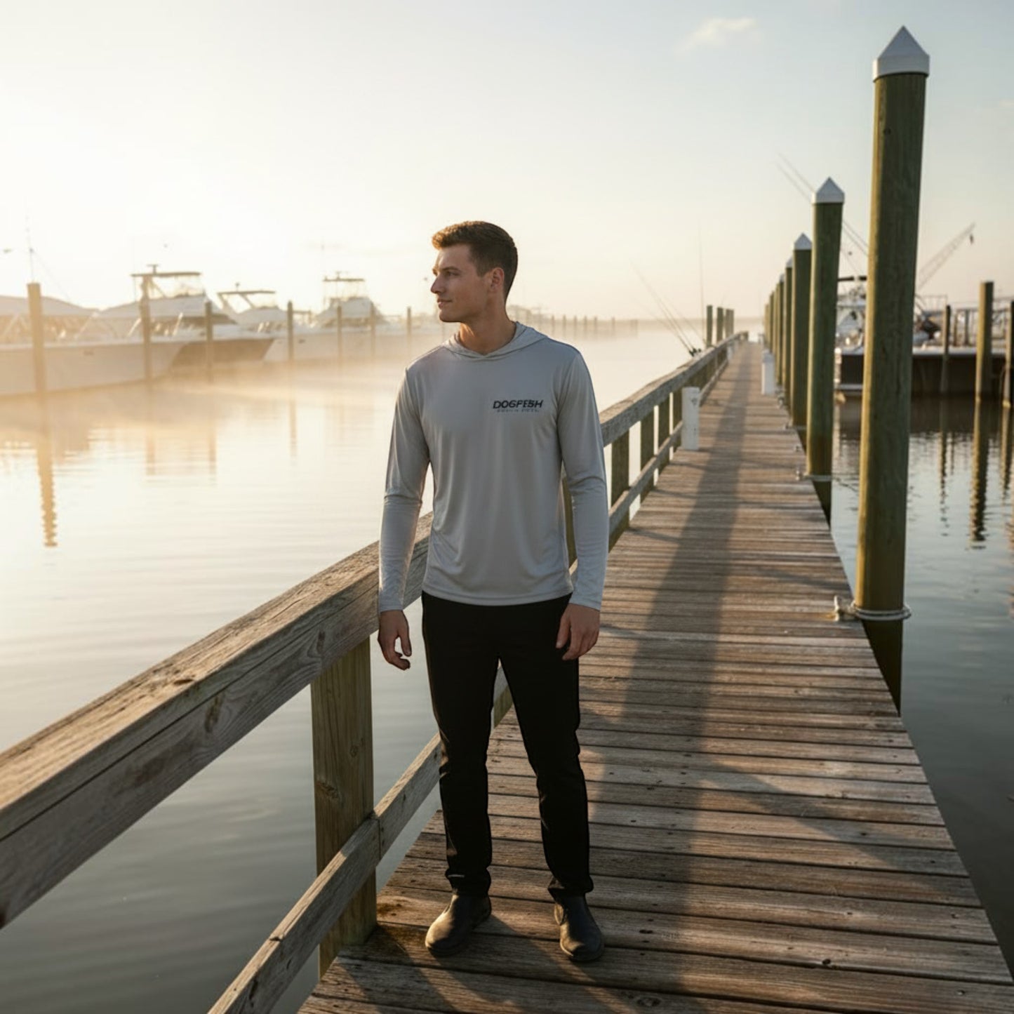 Man standing on a wooden dock wearing a light gray long-sleeve shirt with a brand logo.