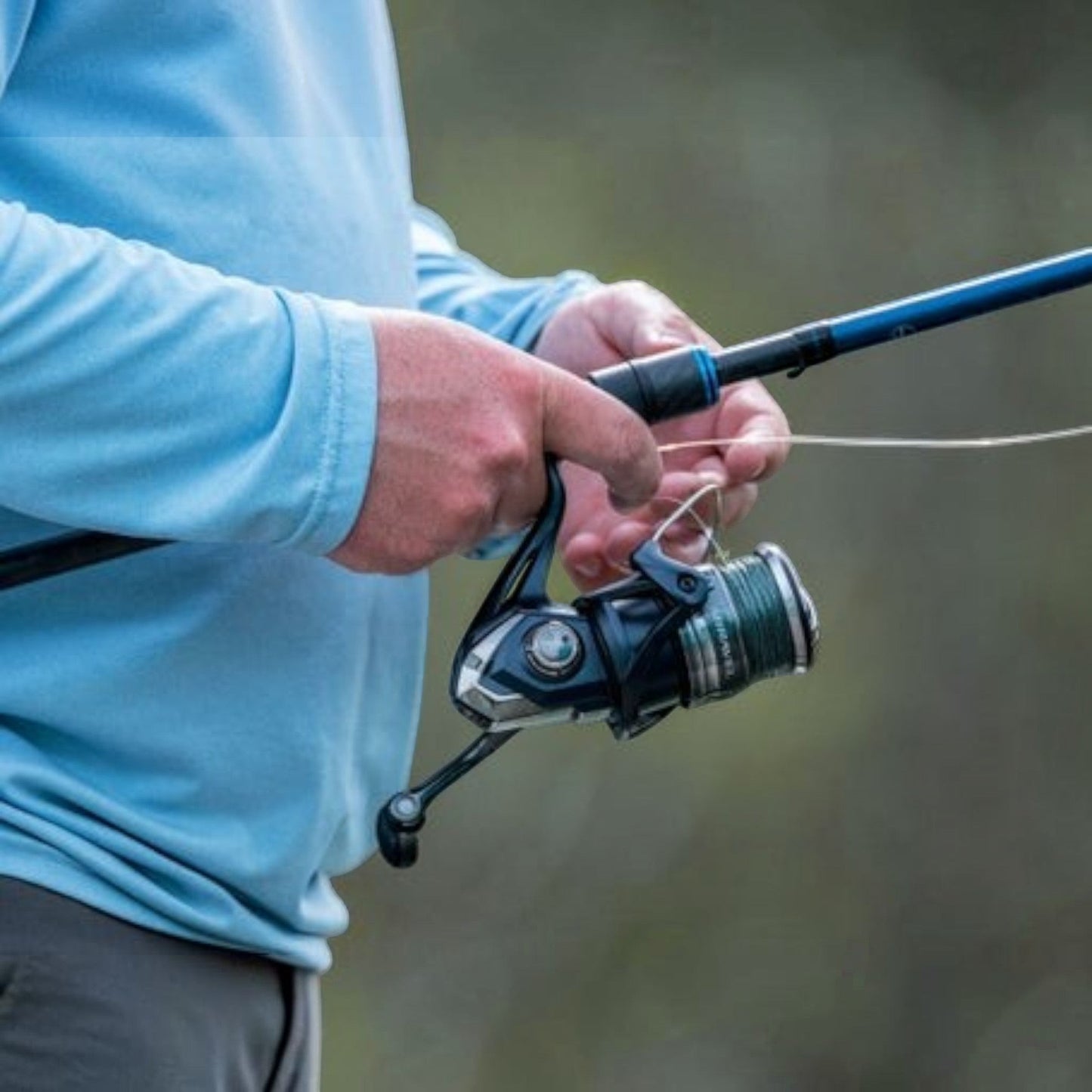 Dogfish Tackle & Marine Shimano Miravel spinning reel, dark blue and silver with green line on spool. Angler holding rod.
