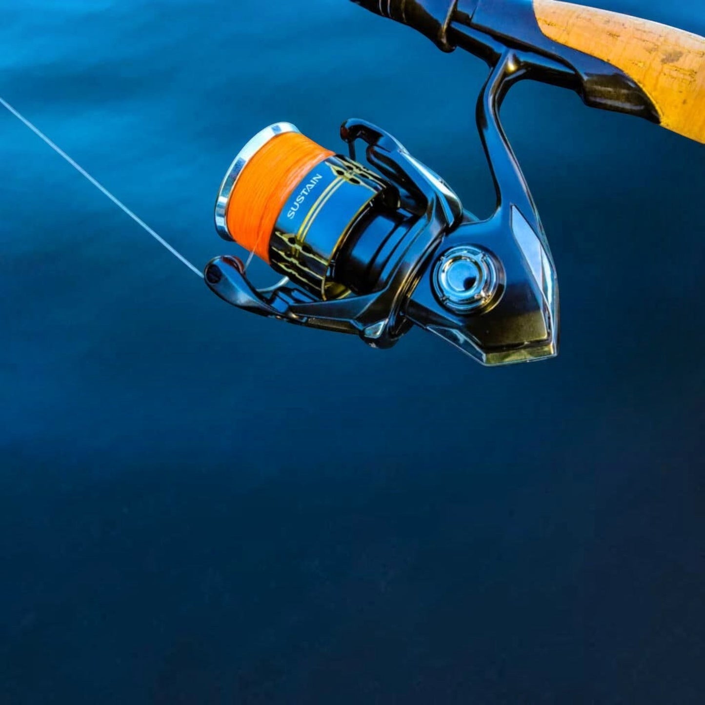 Dogfish Tackle & Marine Shimano Sustain FK spinning reel with orange fishing line on a dark blue water background.