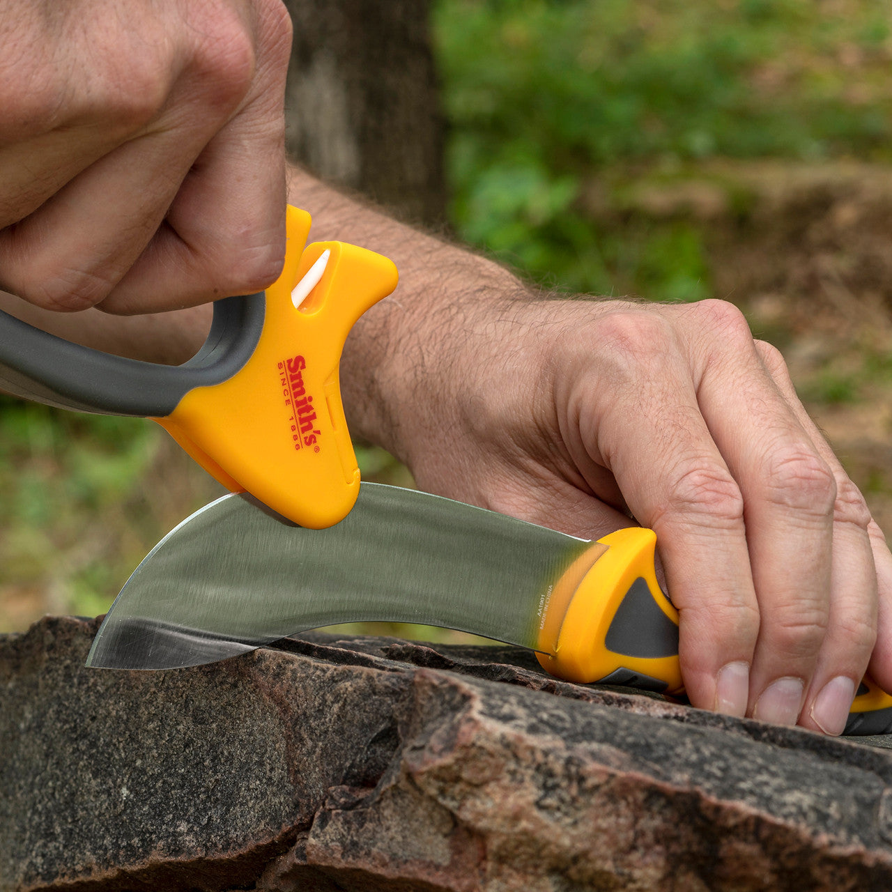 Person using a knife with a yellow handle on a rock outdoors