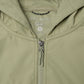 Close-up of a hooded zip-front jacket in a light sage green color, showing the inner neck label with 'PELAGIC' and size 'L'.