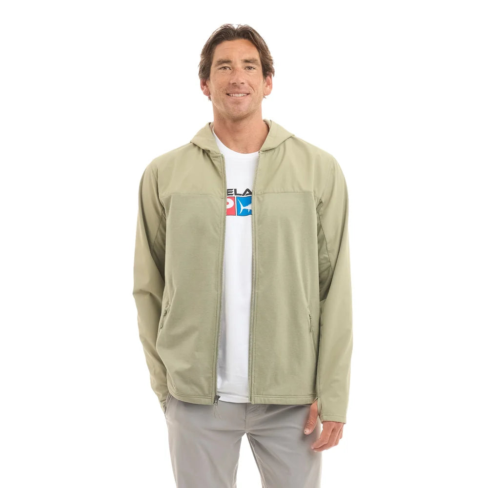 A man wearing a light sage green hooded zip-up jacket over a white graphic t-shirt and gray pants, standing against a plain white background.