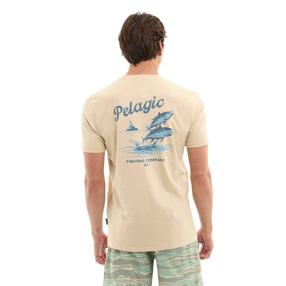A man viewed from behind wearing a beige t-shirt with a blue graphic print of sailboats and fish on the back, paired with green patterned swim trunks, against a plain white background.