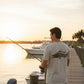 Man fishing on a dock at sunset with a boat and scenic water background.