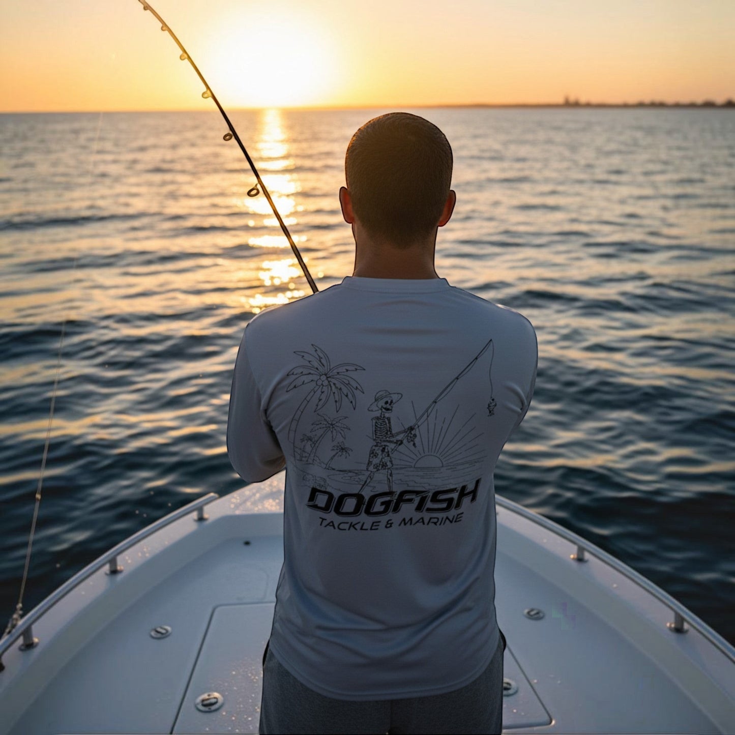 Man on a boat wearing a 'Dogfish Tackle & Marine' shirt with sunset over water.