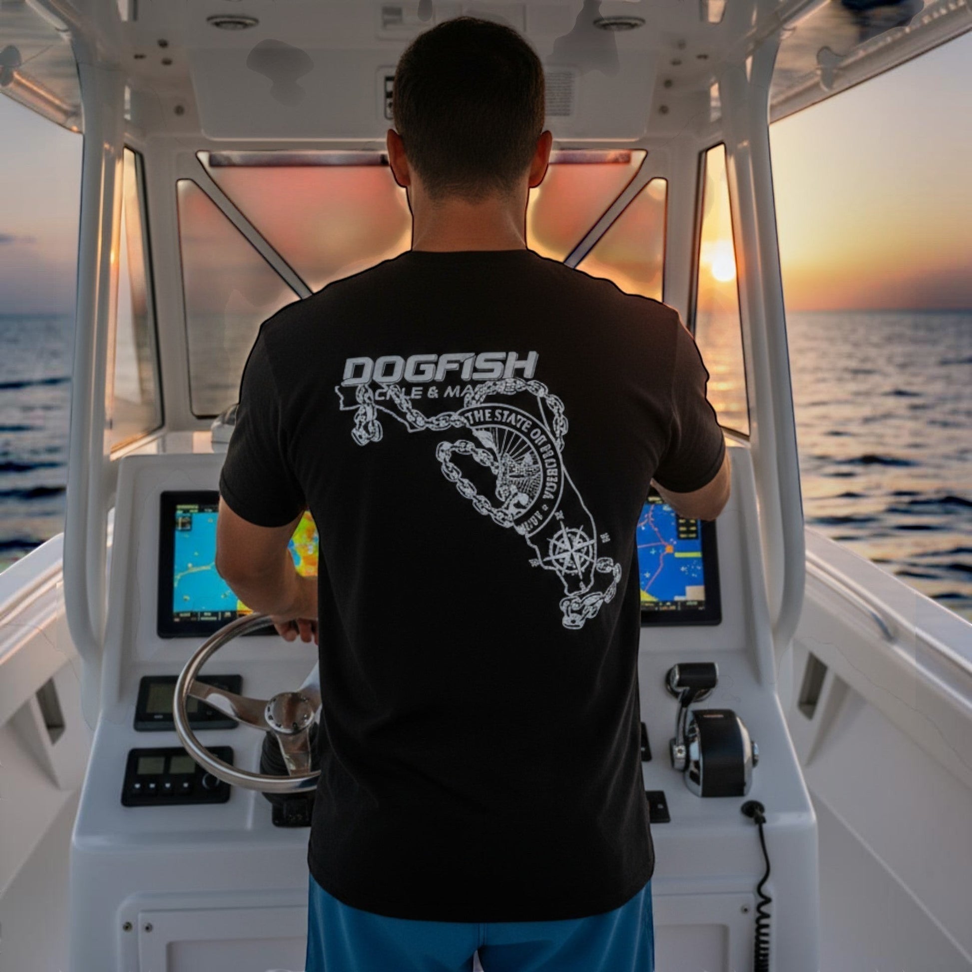 Dogfish Tackle & Marine black poly-cotton t-shirt with Florida Unchained logo on back, worn by man steering boat at sunset.