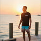 Dogfish Tackle & Marine black short sleeve t-shirt with Florida Unchained logo, worn by a man on a dock at sunset.