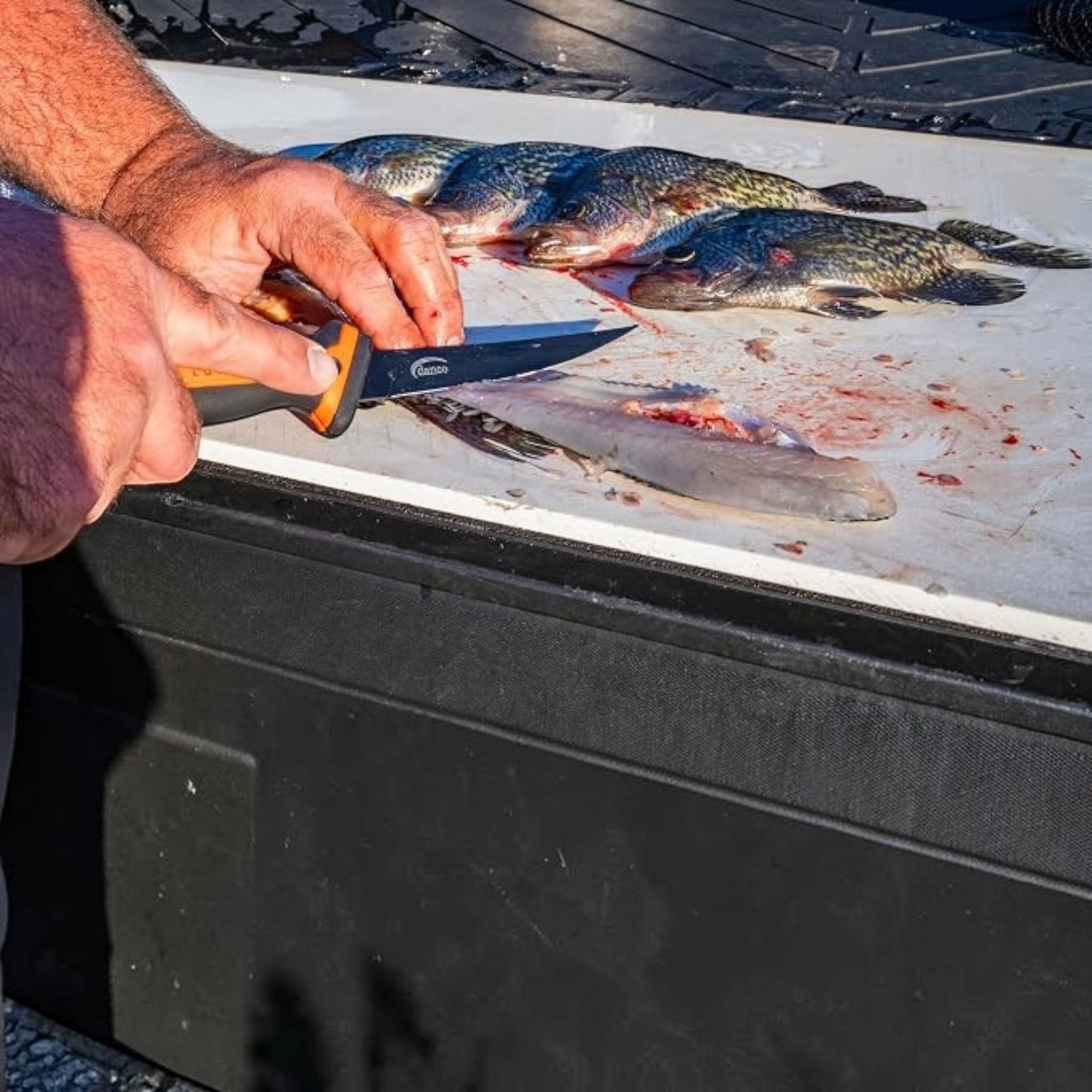 Dogfish Tackle & Marine Danco Lunar-I 6in folding fillet knife with orange and black grip filleting fish on a board