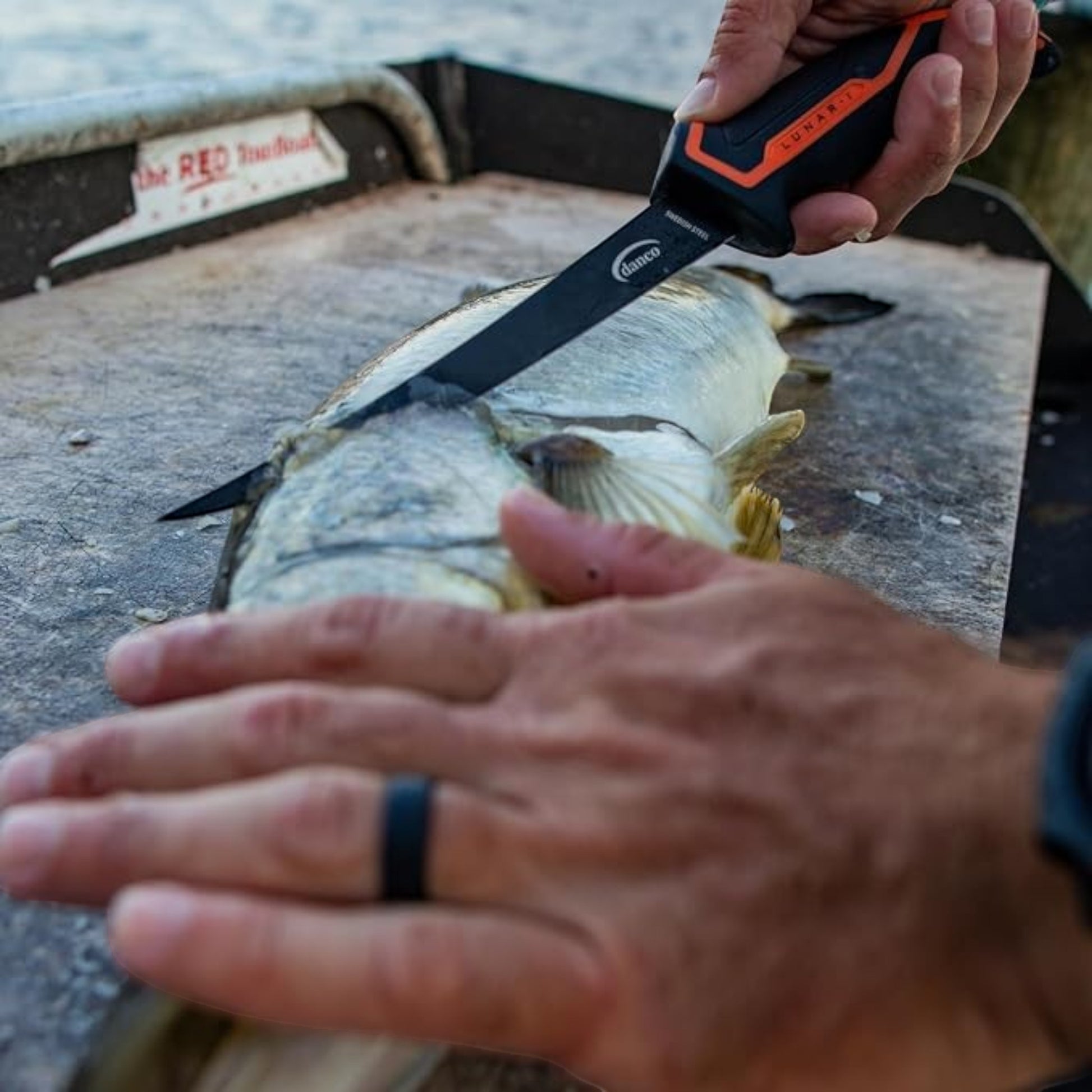 Dogfish Tackle & Marine Danco Lunar-I 7-inch fillet knife with black blade and orange grip filleting a fish on deck