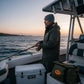 Dogfish Tackle & Marine grey polyester super stretch watch cap with orange leather patch logo, worn by a man fishing on a boat at sunset.