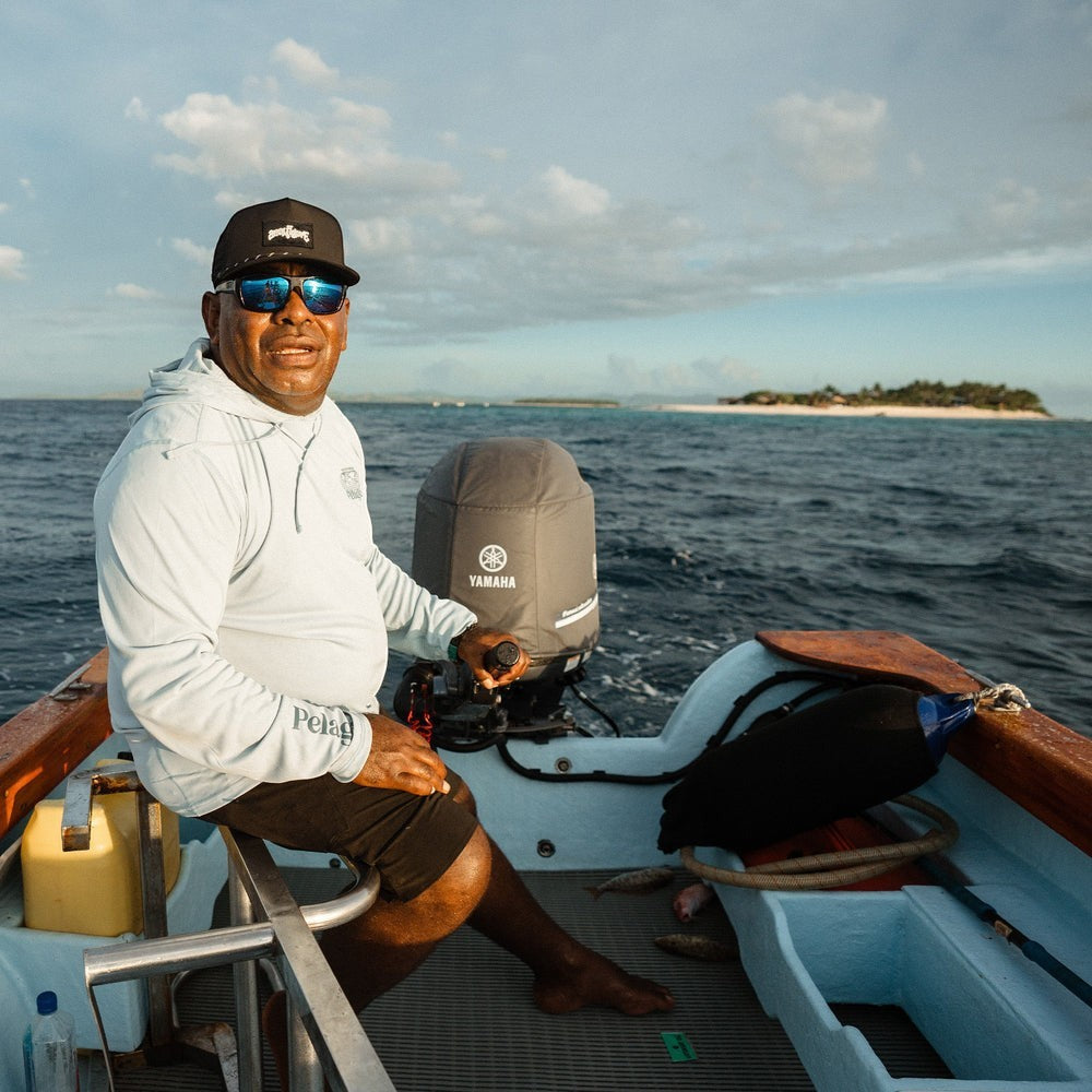 Dogfish Tackle & Marine man wearing a black Pelagic Upswell Stick Figure Hat and light blue long-sleeve shirt on a boat.