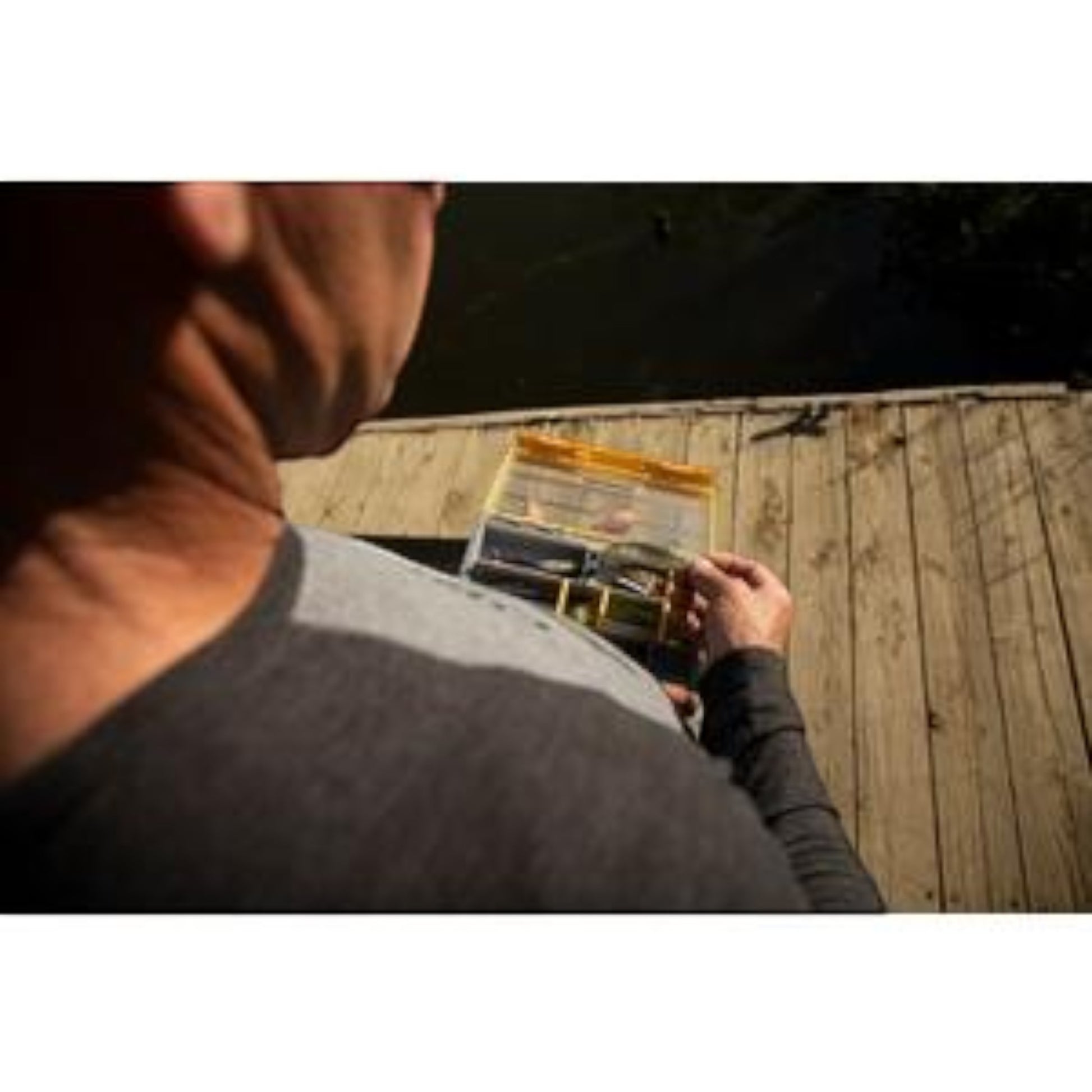 Dogfish Tackle & Marine angler holding a Plano Edge 3500 utility box with fishing lures on a wooden dock