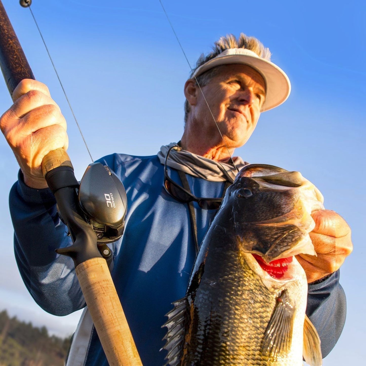 Dogfish Tackle & Marine Shimano Curado DC baitcasting reel in gunmetal grey, held by a man with a large bass.