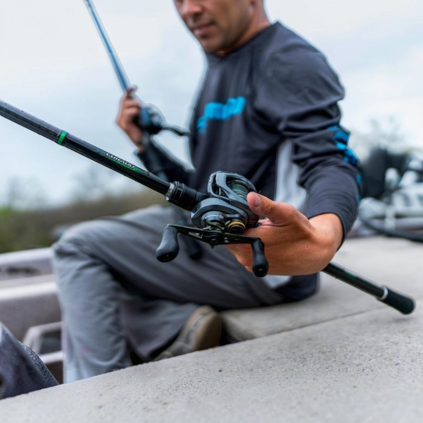 Dogfish Tackle & Marine Shimano Curado DC baitcasting reel in gunmetal grey with black handle, held by a person on a boat.