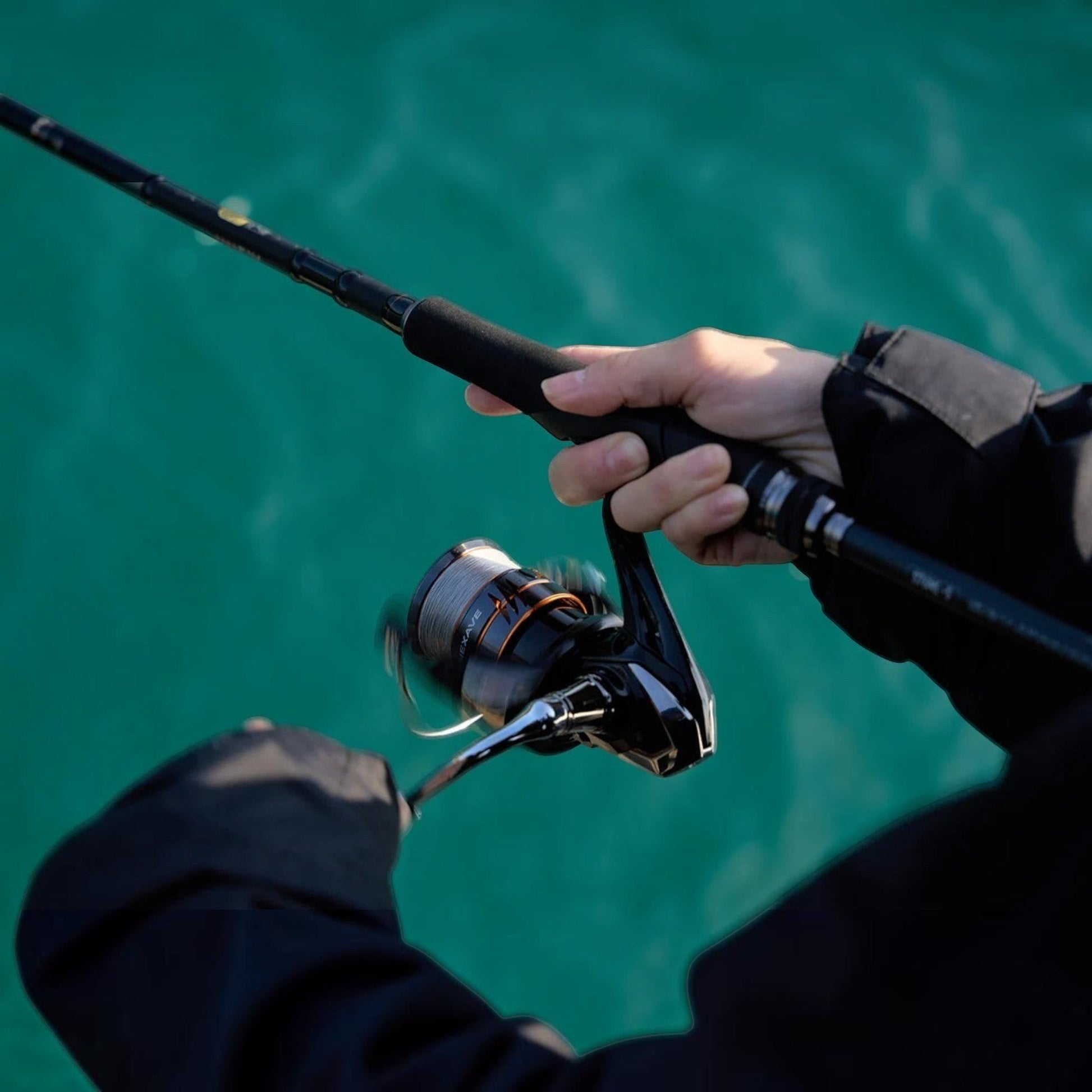 Dogfish Tackle & Marine Shimano Nexave FJ spinning reel with black and orange accents, held by a person fishing in turquoise water.