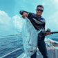 Dogfish Tackle & Marine angler holding a large silver fish on a boat, blue sky with clouds.
