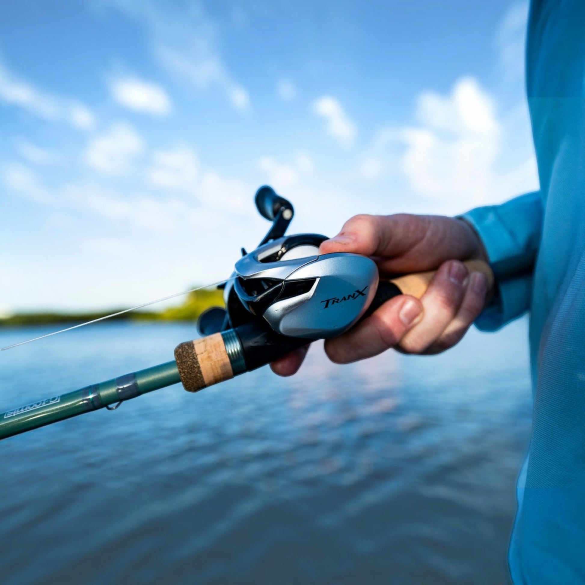 Dogfish Tackle & Marine Shimano Tranx 200 A baitcasting reel, silver and black with cork handle, held by a person fishing.