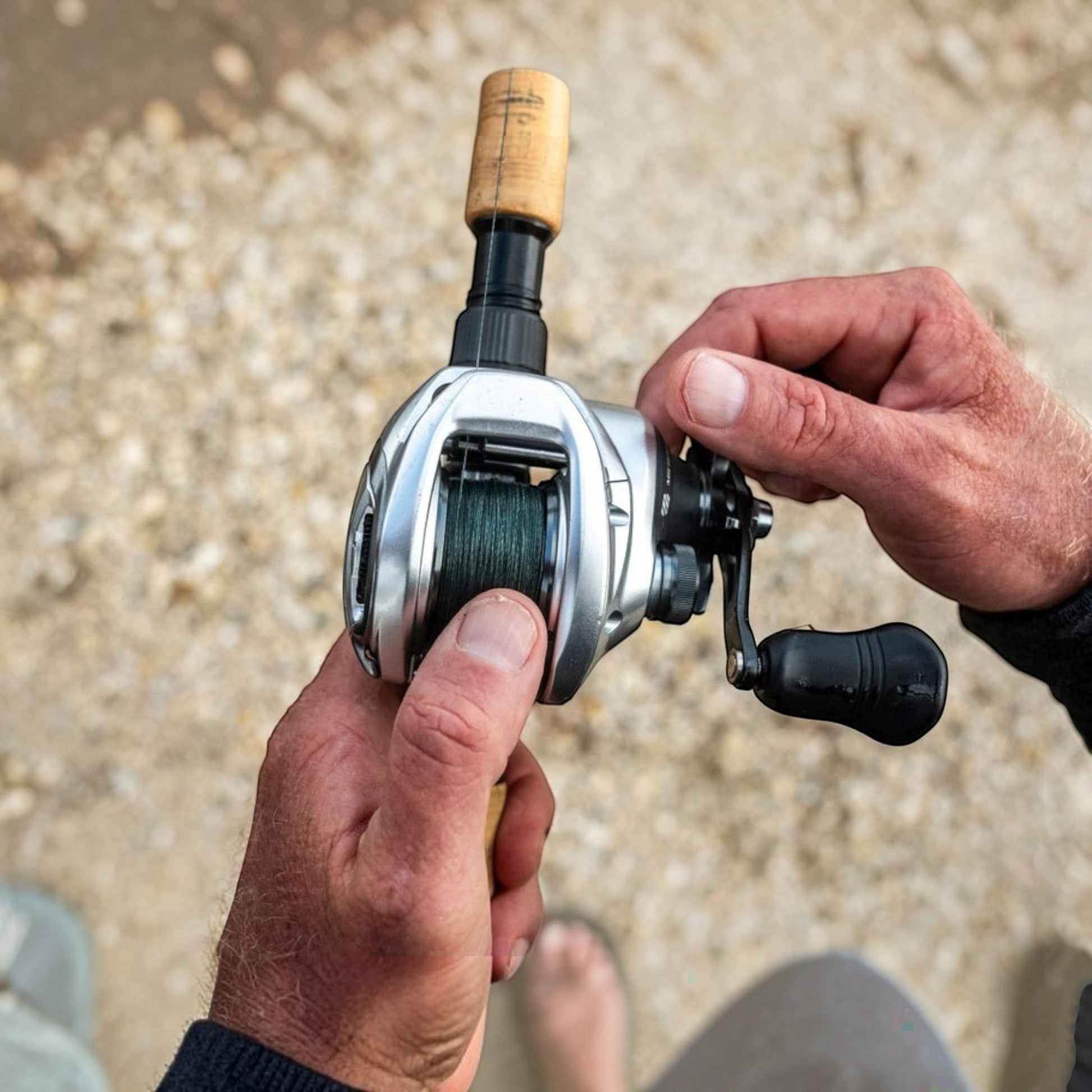 Dogfish Tackle & Marine Shimano Tranx B baitcasting reel, silver with black handle and green line. Close-up of hands holding the reel.