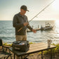 Dogfish Tackle & Marine black trucker hat with embroidered logo, worn by a man fishing by the water.