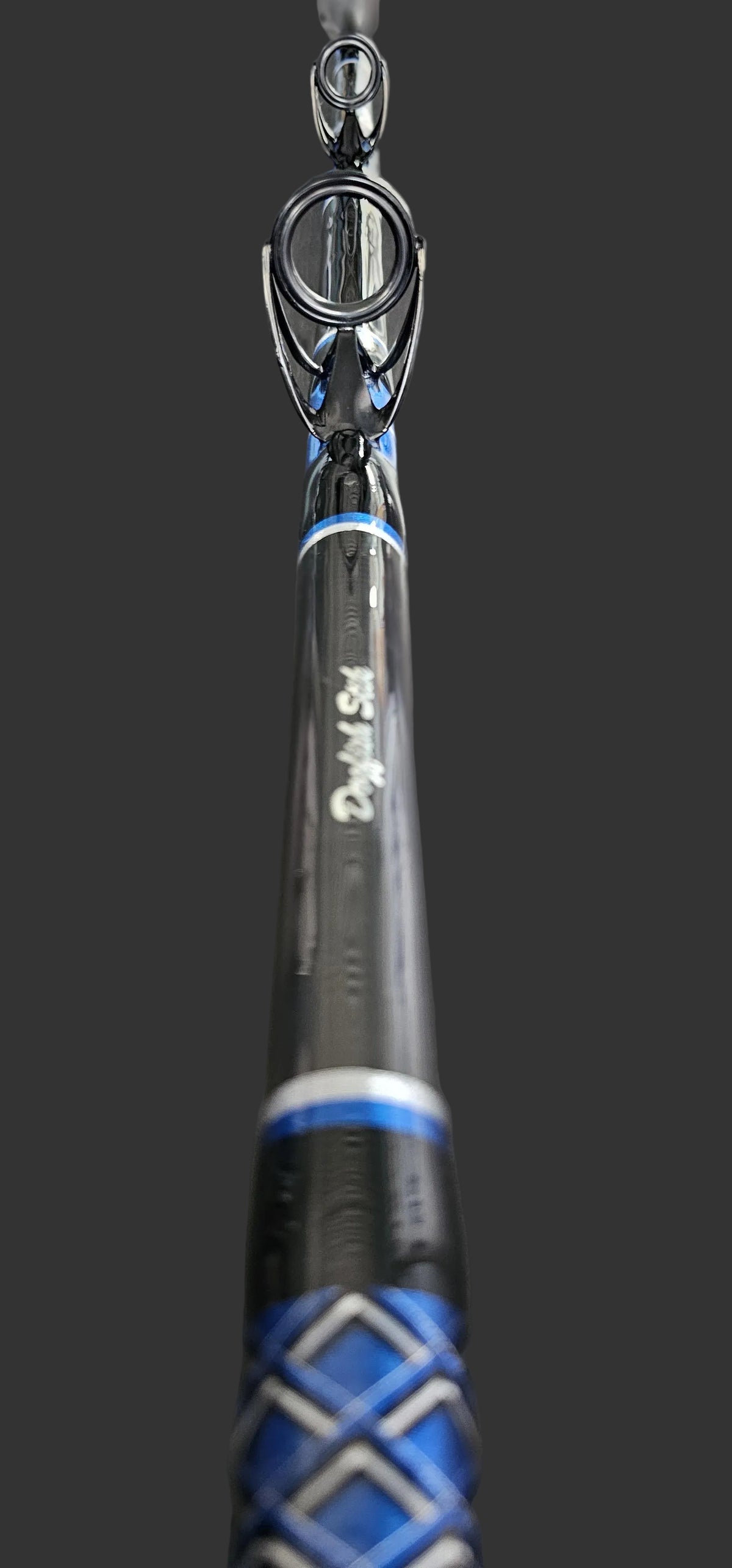 Close-up of a black and blue Dogfish Stik fishing rod with black metal guides, resting on a dark wood surface.