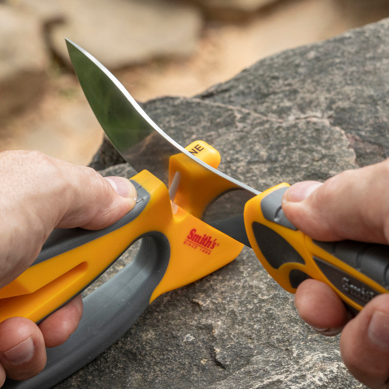 Person holding a knife with a yellow and gray handle on a rock